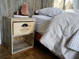 Vu de côté d'une table de chevet en bois avec un tiroir en caisse à vin et une poignet en laiton à côté d'un lit