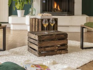 Deux caisses en bois posées sur un tapis blanc devant une cheminée. Deux verres sont posés sur l'une des caisses